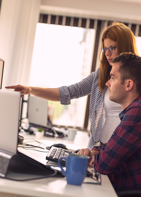 Um homem e uma mulher em frente ao computador trabalhando em conjunto para uma solução.